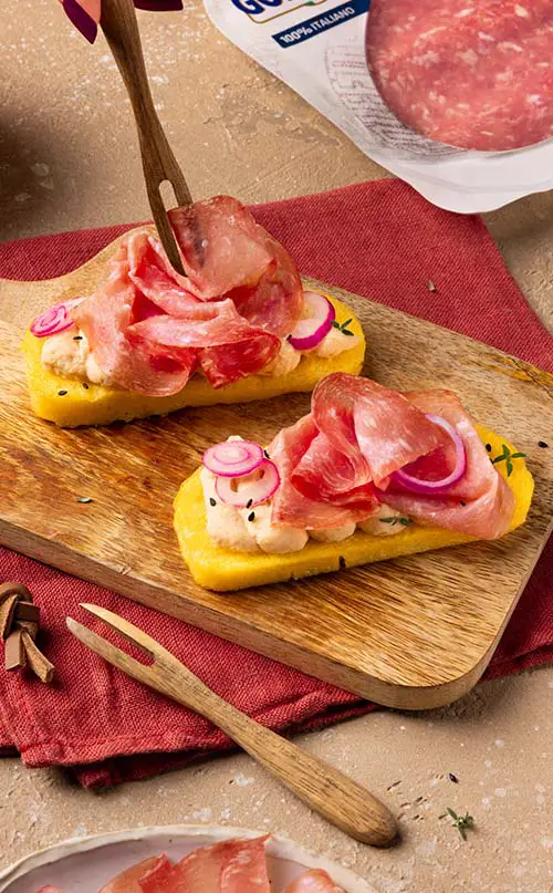 Crostoni di polenta con crema di cannellini, golfetta e cipolla agrodolce su un tagliere